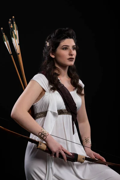 一个身穿白衣 头戴弓箭黑色背景的弓箭手的画像 希腊女神阿耳忒弥斯摄影棚拍摄 黑色长发黑发黑发的专业化妆和发型 — 图库照片