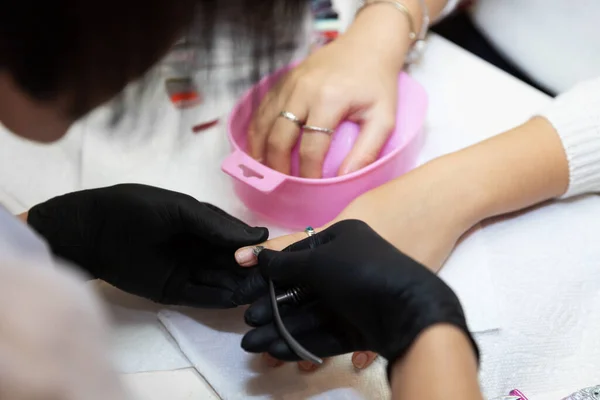 Careful removing of cuticle. Nail care after quarantine. Work of a manicurist in salon. Removing the cuticle with a bath of water and nail clippers. Manicurist in black gloves while working.