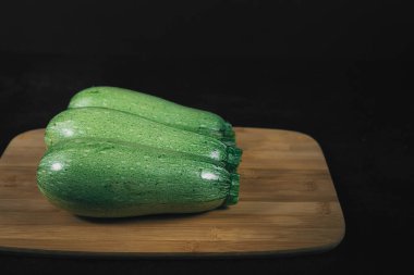 Koyu arkaplanda tahta üzerinde üç yeşil kabak. Organik ekolojik gıda. Sağlıklı beslenme. Taze toplanmış sebzeler. Salata için taze sebzeler. Doğal organik gıda. Yenilebilir sebze arkaplanı. 