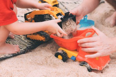 Babalar Günü. Baba ve oğul. Küçük oğlum kumsalda babasıyla oyuncak oynuyor. Sevgi dolu bir aile. Mutlu aile babası ve çocuğu. Oyuncak arabalar. Kumsalda bir adam ve küçük bir çocuğun elleri. Birlikte