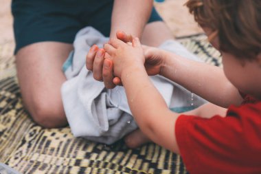Babalar Günü. Baba ve oğul. Baba, oğlunu sahildeki bir şişeden aldığı suyla yıkıyor. Mutlu aile babası ve çocuğu. Genç bir adamın ve oğlunun elleri arka planda bulanıklaştı.