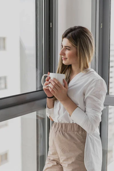 Pencerenin yanında kahve ya da çay içen genç ve güzel bir kadın. Hayal kur ve rahatla. İyi günler. Sabahları kadın elinde bir kupayla güneşin doğuşunu seyrediyor ve harika bir sabah geçiriyor.