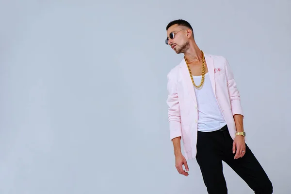 fashionable sophisticated man in a pink jacket and black trousers, wears a gold chain, the manifestation of emotions gestures hands space for text.