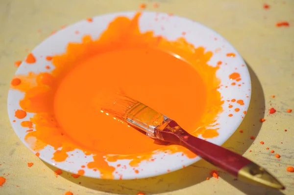 orange paint in a white plate with a brush on an old table.