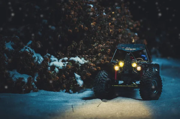 Coche controlado por radio en la nieve por la noche, las luces brillan. Regalo de Navidad rc coche —  Fotos de Stock