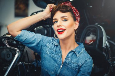 Motosiklet yanında poz veren güzel bir kadın, servis sırasında motosiklet tamir ederken, bir takvim için şık bir görüntü.