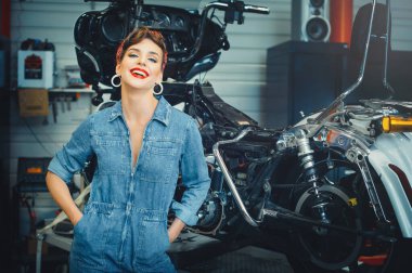 Motosiklet yanında poz veren güzel bir kadın, servis sırasında motosiklet tamir ederken, bir takvim için şık bir görüntü.