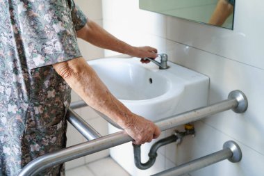 Asyalı yaşlı kadın hasta tuvalette tuvalet desteği kullanıyor..