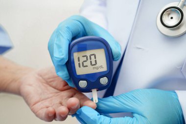 Diyabet tedavisinde kan şekeri seviyesini kontrol etmek için dijital glikoz ölçer kullanan Asyalı doktor.