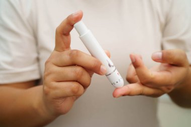 Evde parmak üzerinde dijital mızrakla kan şekeri seviyesini ölçmek için Asyalı kadın kendini test ediyor..