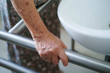 Asyalı yaşlı kadın hasta tuvalette tuvalet desteği kullanıyor..