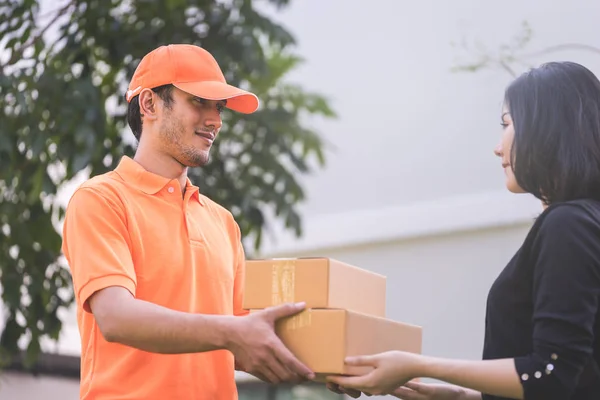 Turuncu elbiseli teslimatçı bir kadına paket teslim ediyor.
