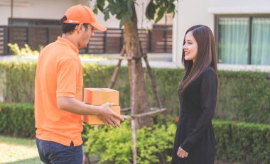 Turuncu elbiseli teslimatçı bir kadına paket teslim ediyor.