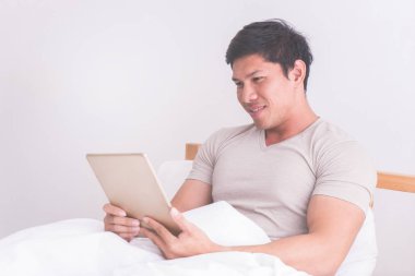 Asyalı erkek beyaz yatağında dijital tablet kullanma