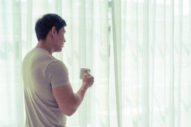 Asyalı adam çay içiyor ve sabah pencerelerine bakıyor.
