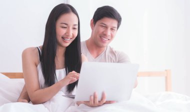 Yataktaki Asyalı çift dizüstü bilgisayar kullanıyor.