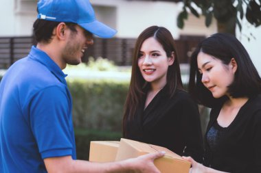 Mavili teslimatçı iki kadına paket teslim ediyor.