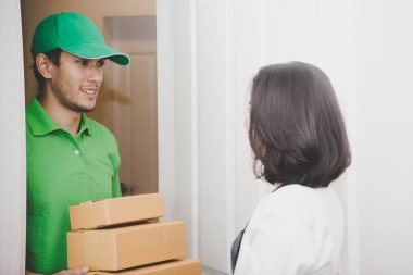 Yeşil elbiseli teslimatçı kadın kapısına paket teslim ediyor.