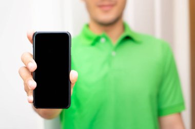 Elinde siyah cep telefonu olan yeşil elbiseli bir erkek işçi.