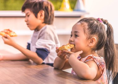 Öğrenci çocuklar sınıfta pizza yiyorlar.