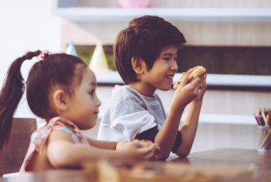 Öğrenci çocuklar sınıfta pizza yiyorlar.