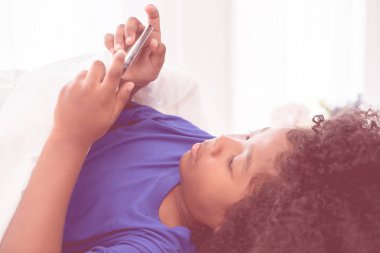 Küçük Afrikalı çocuk yatakta akıllı telefonuyla oynuyor.
