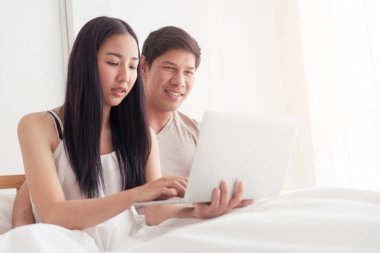 Yataktaki Asyalı çift dizüstü bilgisayar kullanıyor.