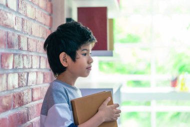 Asyalı çocuk tuğla duvar arka plan üzerinde kitap tutuyor
