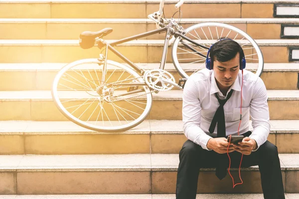 Business man is relaxing listening to music with his bicycle on the side