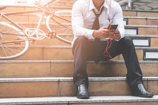 Business man is relaxing listening to music with his bicycle on the side