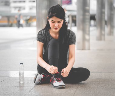 Asyalı kadın koşucu mola veriyor ve ayakkabılarını sıkıyor.