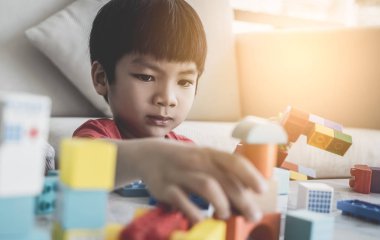 Asyalı çocuk oturma odasındaki masaya oyuncak blokları diziyor.