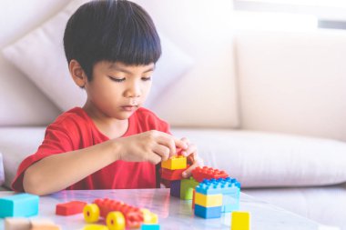 Asyalı çocuk oturma odasındaki masaya oyuncak blokları diziyor.