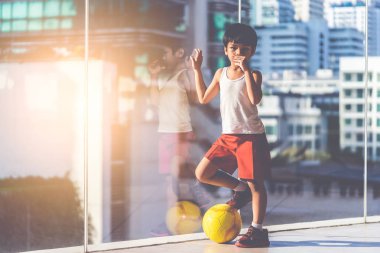 Futbolcu çocuk odada topa basıyor.