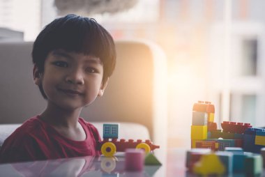 Asyalı çocuk oturma odasındaki masaya oyuncak blokları diziyor.