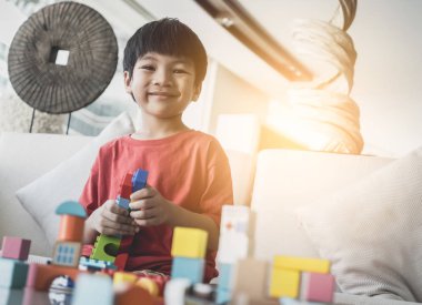 Asyalı çocuk oturma odasındaki masaya oyuncak blokları diziyor.