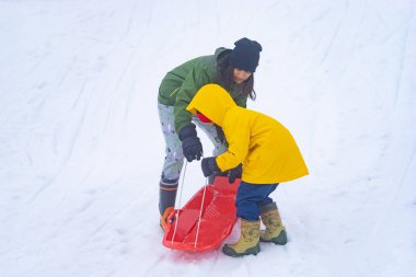 Anne kızına kızak sürmesi için yardım ediyor.