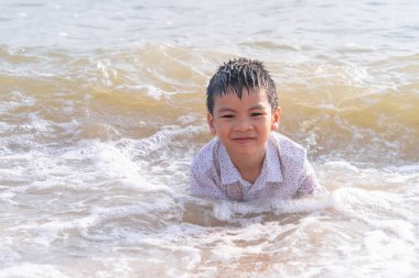 Küçük çocuk Pattaya sahilinde kum ve el sallıyor.