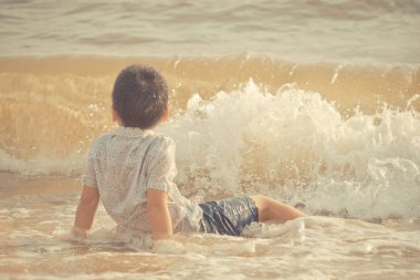 Küçük çocuk Pattaya sahilinde kum ve el sallıyor.