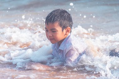 Küçük çocuk Pattaya sahilinde kum ve el sallıyor.