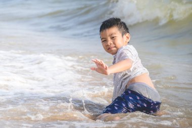 Küçük çocuk Pattaya sahilinde kum ve el sallıyor.