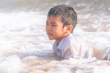 Küçük çocuk Pattaya sahilinde kum ve el sallıyor.