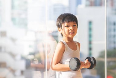 Küçük çocuk pencere şehrinin yanında dambılla çalışıyor..