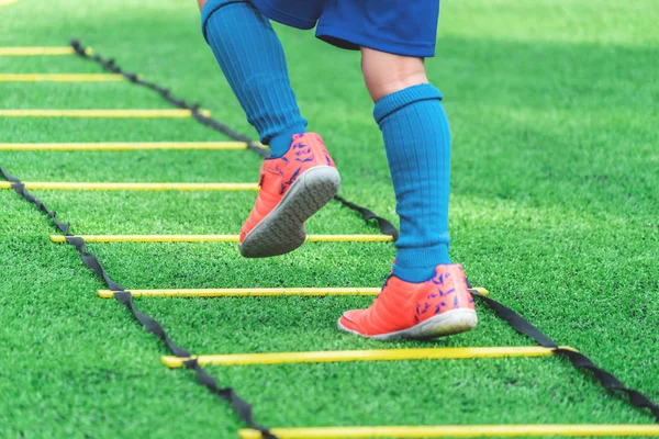 Child feet with soccer boots training on agility speed ladder in