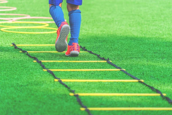 Pieds d'enfant avec des bottes de football formation sur l'agilité échelle de vitesse dans — Photo