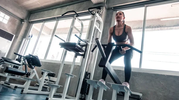 La mujer está levantando peso en la máquina de entrenamiento en cuclillas — Foto de Stock