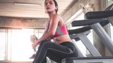 Kadın spor salonunda koşu bandında su içiyor.