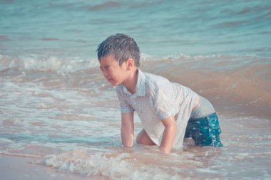 Küçük çocuk Pattaya sahilinde kum ve el sallıyor.