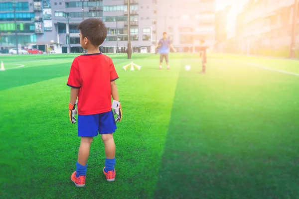 Kaleci eldivenli küçük çocuk antrenman sahasında duruyor.