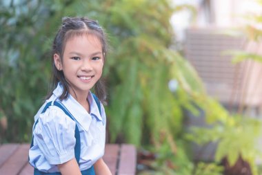 Mutlu Asyalı öğrenci yeşil bahçede oturuyor.